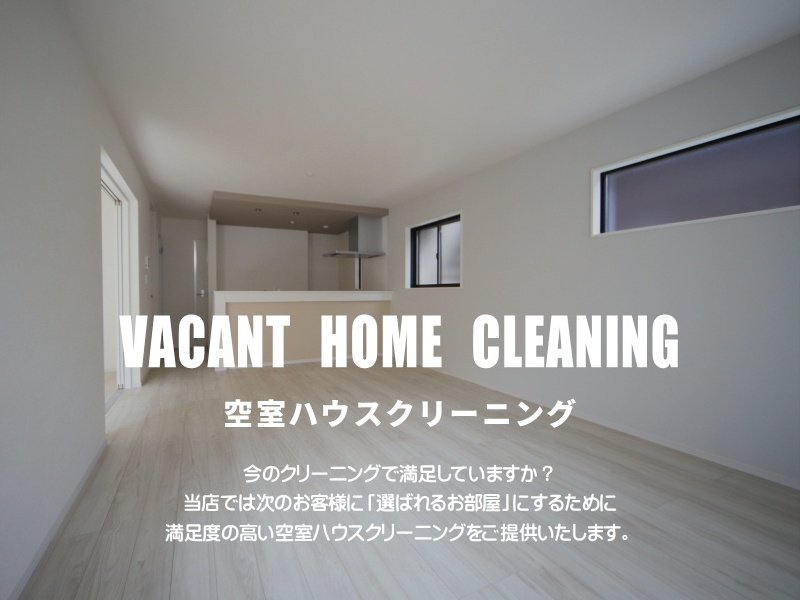 清潔で広々とした空室の住宅のリビングルーム。フローリングの床と白い壁、奥にはキッチンが見える。
